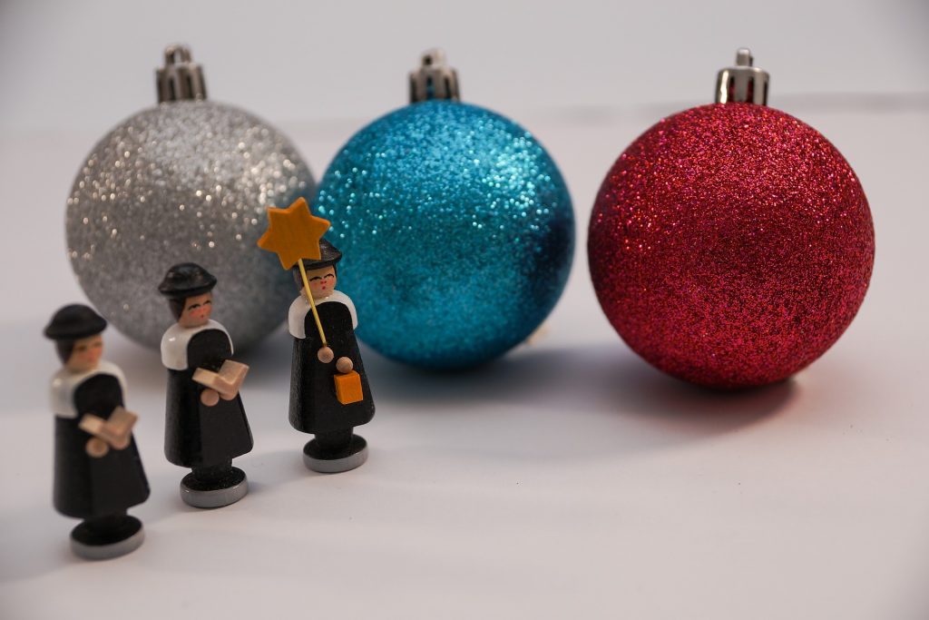 Several small puritan figurines arranged in front of three much larger glitter-covered Christmas ornaments