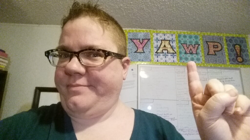 A photo of me pointing to one of my art therapy pieces, a large banner with adult coloring book pages printed with the letters Y, A, W, P, and an exclamation point. 